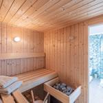 Sauna mit Holzwand und Bank. Durchgang zu Dusche mit blauem Mosaik.