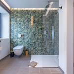 Badezimmer mit Dusche, WC und Fenster. Wandfliesen mit tropischem Motiv.