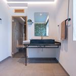 Badezimmer mit Waschtisch, Spiegel und Sauna im Hintergrund.
