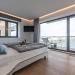 Schlafzimmer mit Balkon, großes Bett und TV. Blick auf Wasser.