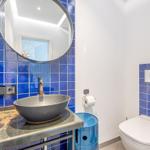 Badezimmer mit blauen Fliesen, runden Spiegel und Waschbecken auf Metallplatte.