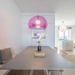 Esszimmer mit langer Tischplatte, pinker Hängelampe und Sitzbank an der Wand.