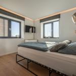 Schlafzimmer mit Bett, zwei Fenstern und Hängelampen.