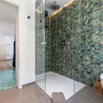 Bad mit Dusche, Toilette und grünem Fliesenboden. Küche und Essbereich sichtbar.