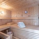 Sauna mit Holzbank, Handtuchstapel und Thermometer an der Wand.