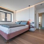 Schlafzimmer mit Bett, Fenster und Holzboden. Gelber Stuhl und Wandspiegel sichtbar.