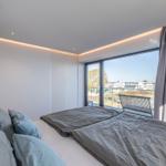 Schlafzimmer mit Blick auf Balkon und Stadt. Bett, Lampe und Vorhänge sind sichtbar.