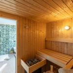 Sauna mit Holzbank und Holzwand. Durchgang zur Dusche mit Glaswand.