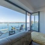 Wohnbereich mit Blick auf Wasser und Terrasse mit Sitzmöbeln.