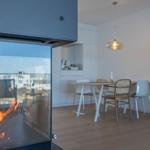 Kamin mit Flamme im Vordergrund, dahinter Essbereich mit Tisch und Stühlen.