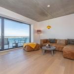 Wohnzimmer mit Blick auf Wasser, braunes Sofa und Holzboden.