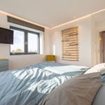 Schlafzimmer mit Bett, TV und Fenster. Holzregal mit Haken an der Wand.