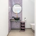 Badezimmer mit Lavendelwand, runden Spiegel und schwarzer Waschschale.