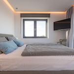 Schlafzimmer mit Doppelbett, Fenster und Wandfernseher.