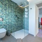 Bad mit Dusche und tropischen Fliesen. Roter Kühlschrank im angrenzenden Raum.