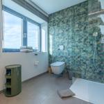 Badezimmer mit Dusche, Toilette und Fenster. Wandfliesen mit tropischem Muster.