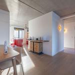 Eingangsbereich mit Holzboden und Tisch. Küche mit roten Schränken. Wandbeleuchtung und Durchgang.