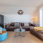 Wohnzimmer mit Ledersofa, blauem Sitzkissen und Blick auf Balkon