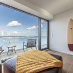 Raum mit Blick auf Wasser, Balkon mit Stühlen und Tisch, Surfbrett an Wand