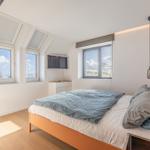 Schlafzimmer mit Dachfenstern, Bett und Fernseher.