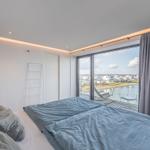 Schlafzimmer mit Blick auf Wasser und Terrasse mit Liegestuhl.