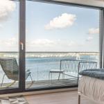 Schlafzimmer mit Blick auf Wasser und Terrasse mit Stuhl und Tisch.