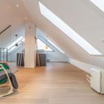 Dachgeschoss mit Holzboden, Dachschrägen, Dachfenstern und kleinem Kühlschrank.