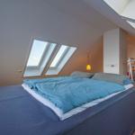 Schlafzimmer mit Dachschrägen, Dachfenster und Bett mit blauer Bettwäsche.
