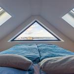 Schlafzimmer mit Dachfenstern und Blick auf Wasser und Gebäude.