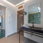 Badezimmer mit Waschtisch, Spiegel und Dusche. Tür führt in Wohnbereich.