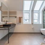 Badezimmer mit Dusche, Toilette und Waschbecken unter Dachfenstern.