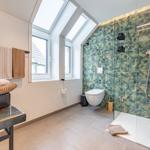 Badezimmer mit Dusche, Toilette und Fenster. Wand mit tropischen Motiven.