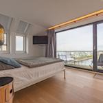 Schlafzimmer mit Balkon und Seeblick. Bett, TV und Holzboden.