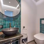Badezimmer mit Waschbecken, Spiegel und Toilette. Wandfliesen in Türkis.