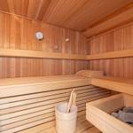 Holzsauna mit Sitzbänken, Steinmulde und Thermometer an der Wand.