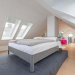 Schlafzimmer mit Dachfenstern, Bett und Sitzgelegenheit.