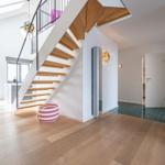 Eingangsbereich mit Holztreppe, Sitzkissen und moderner Beleuchtung.