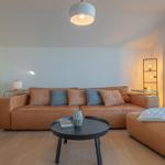 Ein Wohnzimmer mit braunem Ledersofa, runden Tisch und grünem Kühlschrank.