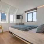 Schlafzimmer mit Bett, Fenstern und gelber Stuhl.