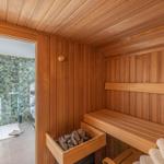 Sauna mit Holzbank und Steinmulde. Durchgang zur Dusche mit tropischen Fliesen.