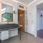 Bad mit Waschbecken, Spiegel und Sauna. Durchgang zu Wohnbereich mit Treppe.