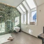 Badezimmer mit Dusche, Toilette und Waschtisch unter Dachfenstern.