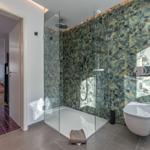 Badezimmer mit Dusche und Toilette, Wandfliesen mit tropischem Motiv.