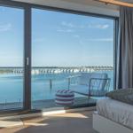 Schlafzimmer mit Blick auf Wasser und Hafen. Balkon mit Sitzmöbeln und Bett.