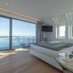 Schlafzimmer mit Blick auf Hafen und Booten. Bett, TV und Glas-Tisch.