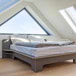 Schlafzimmer mit Dachschrägen, großem Fenster und Bett mit weißen Kissen.
