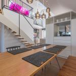 Essbereich mit Holztisch, Stühlen und Platten. Hintergrund: Treppe und Küchenzeile.