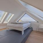 Schlafzimmer mit Dachfenstern und weißem Bett. Holzboden und Stuhl sind sichtbar.