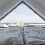 Zwei Betten unter einem Dreiecksfenster mit Blick auf Wasser und Gebäude.