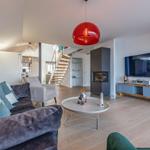 Wohnzimmer mit Sofa, Fernseher und Kamin. Rote Deckenlampe und Holzboden.